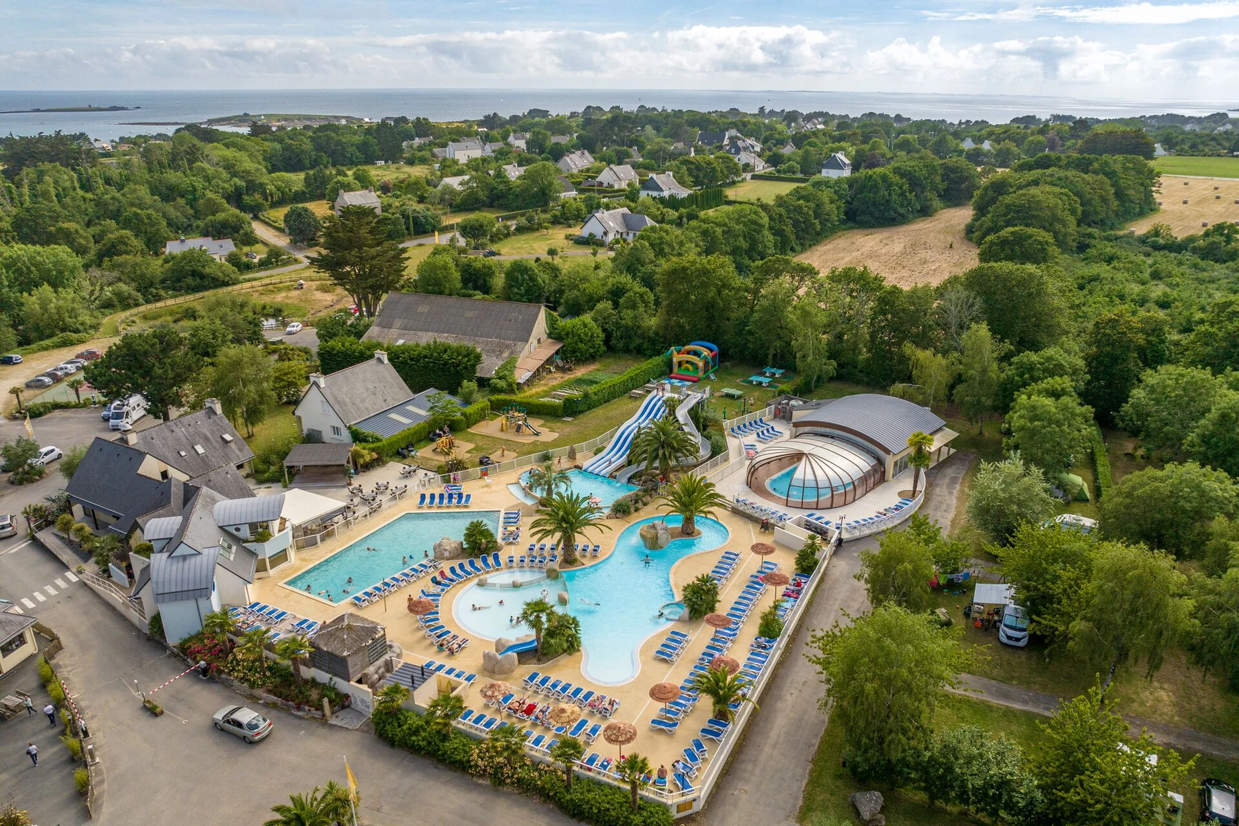 Swimming pools and water slides surrounded by lounge chairs; set within a lush, green campsite near the sea at Les 2 Fontaines
