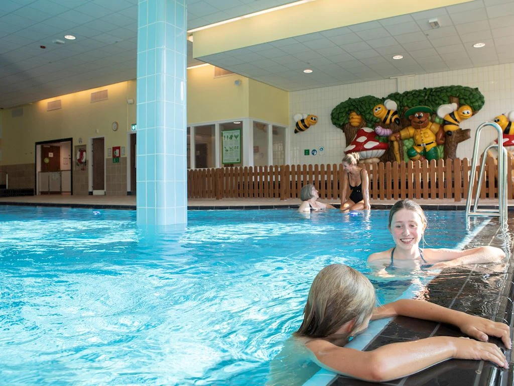 People swim in an indoor pool near colorful cartoon decorations and a wooden fence at Landal Winterberg