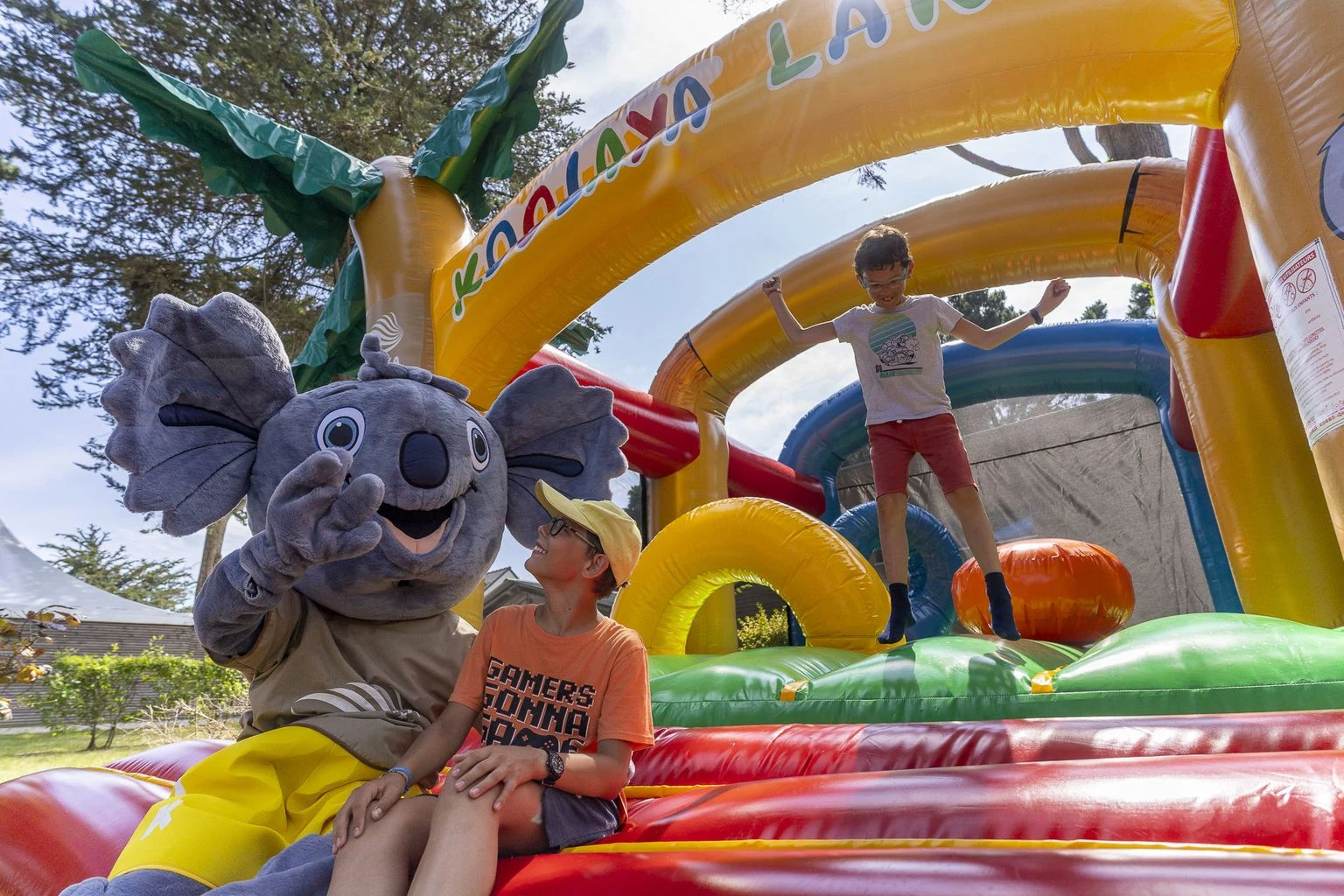 Person in a koala suit sitting with a child, another child jumping on an inflatable structure at Moulin de l'Eclis