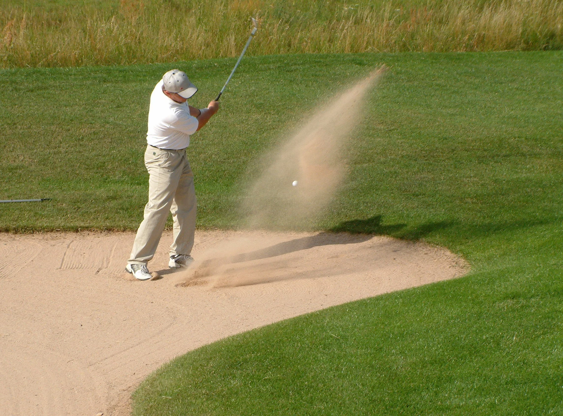 Golfer striking ball from bunker, sand flying, on green golf course at KNAUS Campingpark Hünfeld