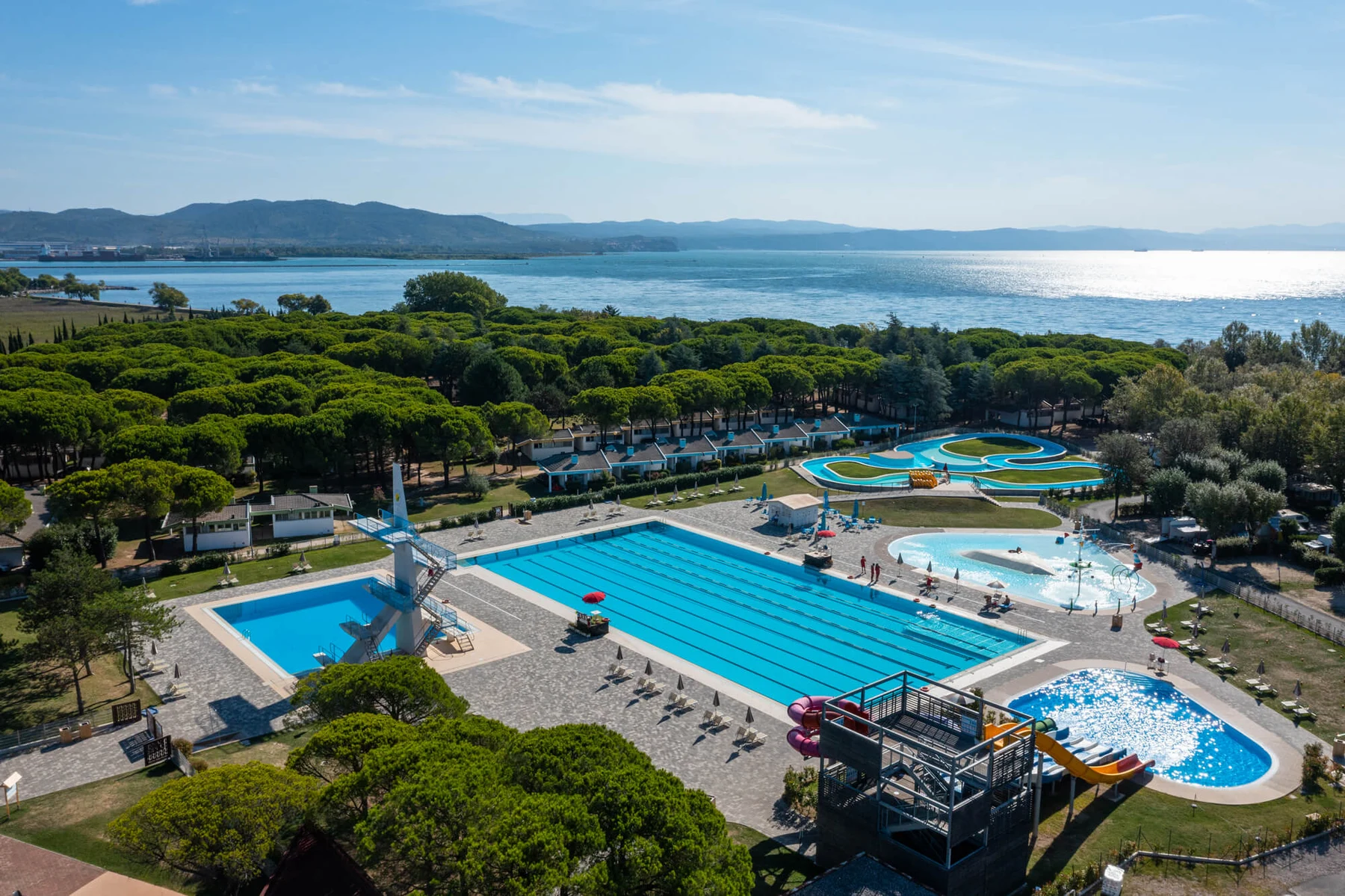 Swimming pools surrounded by trees and play areas; distant lake and mountains at Marina Julia Family Camping Village