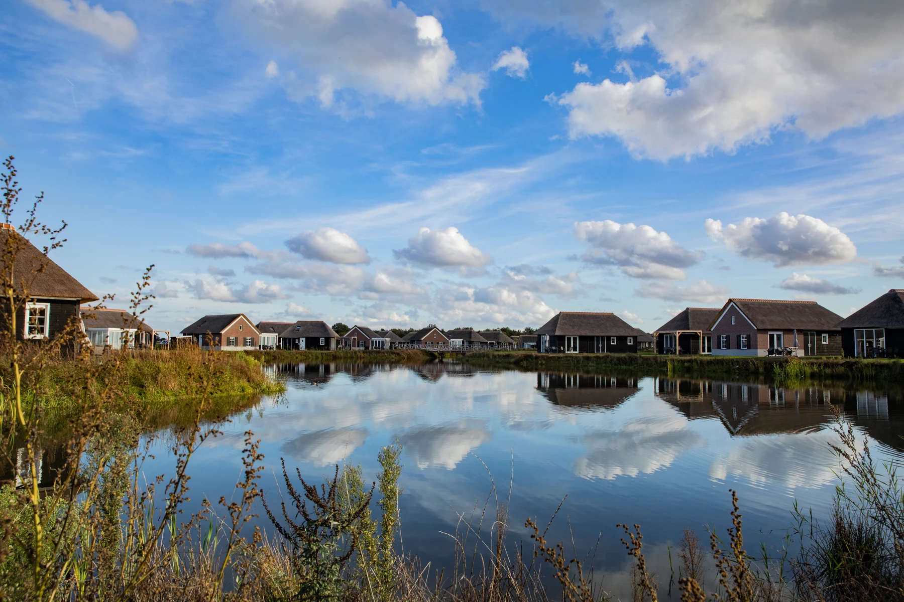 Small cottages lining a tranquil lake, reflecting in the water under a partly cloudy sky at De Heihorsten