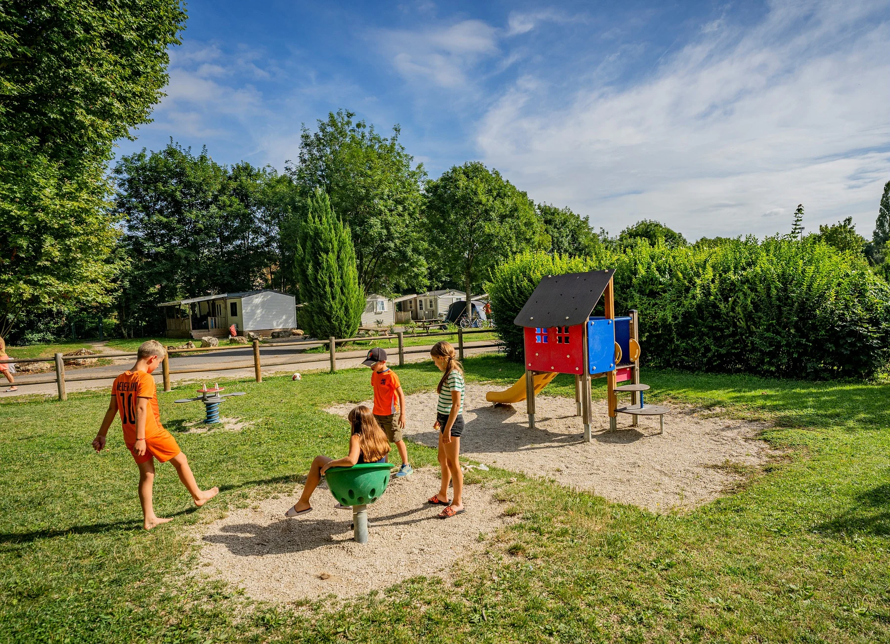 Children play on playground equipment surrounded by greenery and mobile homes at Marvilla Parks Paris Est