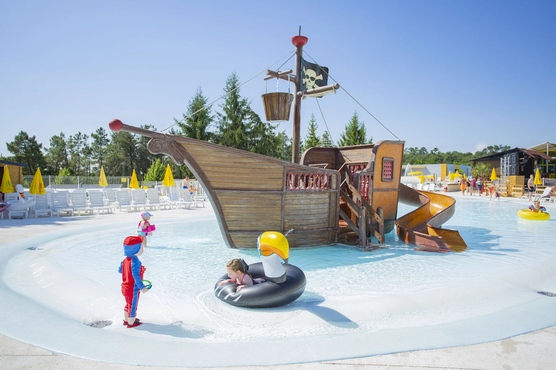 Children playing on a pirate ship-themed water slide in a shallow pool surrounded by lounge chairs and umbrellas at Le Grand Dague