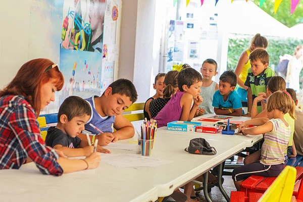 Children drawing and coloring around a table, supervised by an adult, in an outdoor covered area at Marvilla Parks Club Le Napoléon