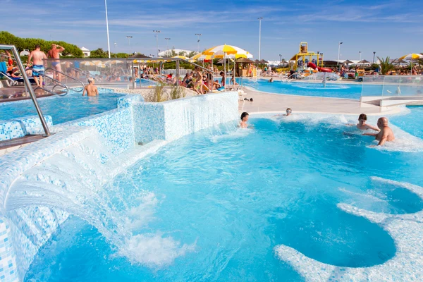 People swimming and relaxing in a large outdoor pool with cascading water and sun umbrellas at Internazionale