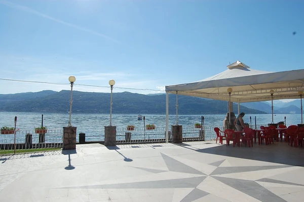 Pavilion with red chairs overlooks a lake with a mountainous backdrop, framed by lamp posts - at Lido di Monvalle