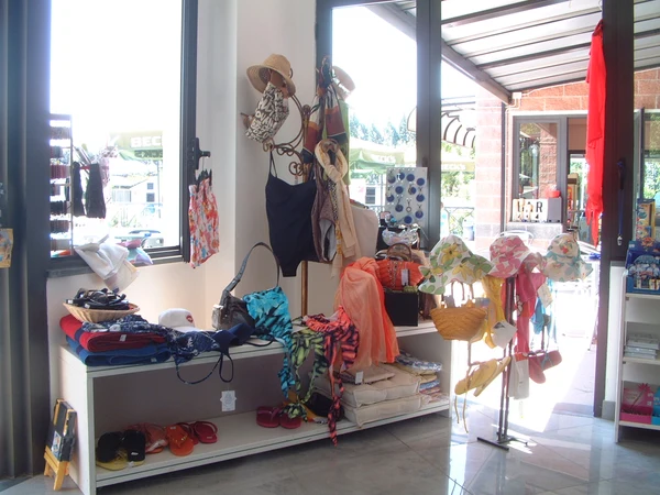Store display showcasing beachwear and swimwear, including hats, bags, swimsuits, and sandals, arranged beside large windows at Village Torre Pendente