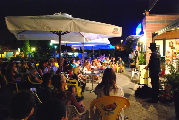 Magician performing under large umbrellas, surrounded by seated audience at night at Village Torre Pendente