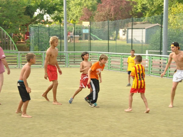 Children playing soccer on a fenced grassy field, surrounded by greenery and park amenities at l'Évasion