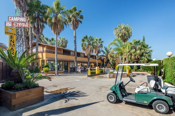 Golf cart parked by palm trees and a building in a sunny campsite entrance at Enmar