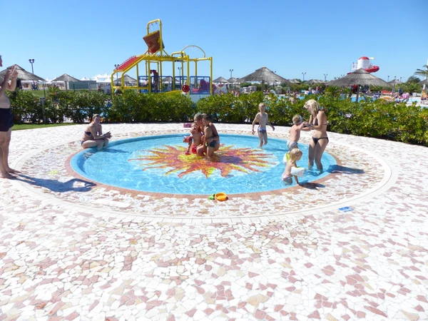 Children playing in a small round pool, with adults supervising, surrounded by a waterpark with slides and greenery at Internazionale
