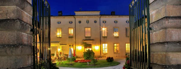 Illuminated building viewed through open wrought-iron gates with tables and chairs arranged in a landscaped garden at Château de l'Epervière