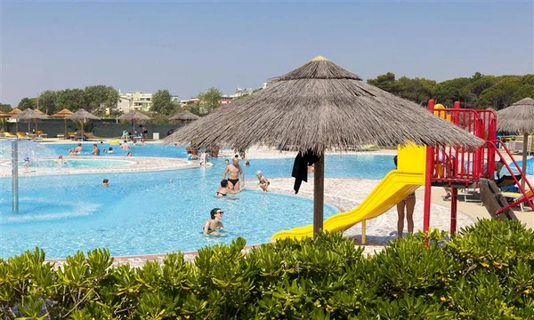 People swimming and playing near pool slides surrounded by greenery and thatched umbrellas at Internazionale