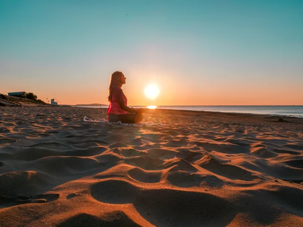 Person meditating on sandy beach during sunrise or sunset, with calm sea and distant buildings in the background at Les Mediterranées Nouvelle Floride