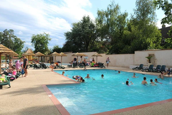 People swimming in an outdoor pool with lounge chairs and straw umbrellas, surrounded by trees and a wall at Château de l'Epervière
