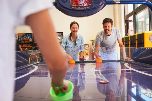 Two adults playing air hockey with a child in an indoor arcade setting at Les Méditerranées Beach Garden