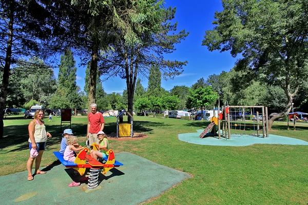 Children playing on a seesaw while adults watch; lush, green park with additional playground equipment and camping tents at Château de l'Epervière