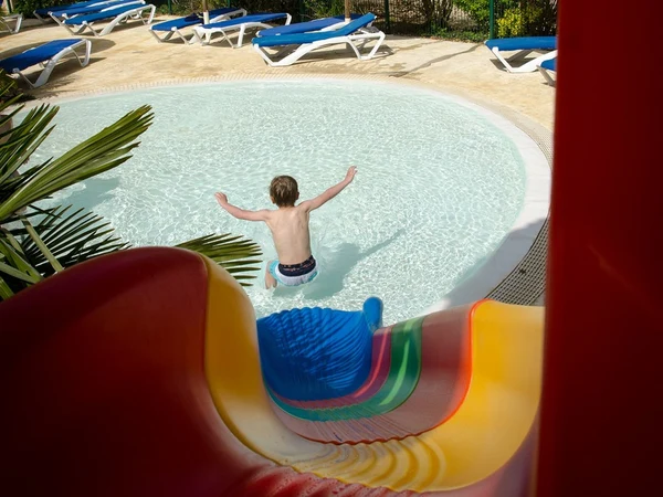 Person splashing into shallow pool after sliding down a colorful waterslide, surrounded by sun loungers in a landscaped area at l'Évasion