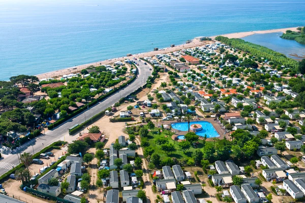 Aerial view of a beachside campsite with mobile homes, a road, a pool, and the ocean in the background at El Pinar