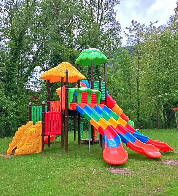 Playground structure featuring colorful slides, set in a grassy area surrounded by tall, leafy trees at Glamping II Borgo delle Arti