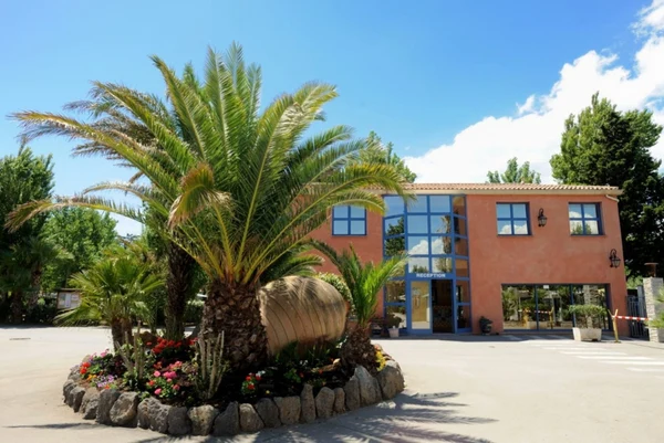 Large building entrance surrounded by palm trees and flowers in a sunny outdoor area at Les Mediterranées Nouvelle Floride