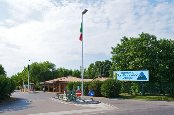 Flagpole with Italian flag standing in front of a building entrance surrounded by greenery and street signs at San Francesco