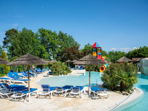 Sun loungers and straw umbrellas surrounding a swimming pool with colorful water slides, amidst trees and blue sky at l'Évasion