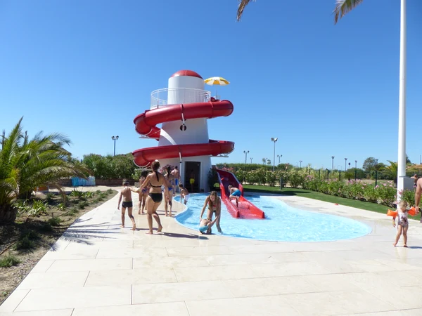 Children playing in a pool area with a red waterslide tower under a clear blue sky, surrounded by plants at Internazionale