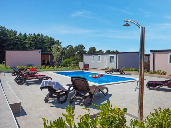 Pool surrounded by lounge chairs and cabins, set in a sunny, outdoor camping area with greenery and trees at Kastanija