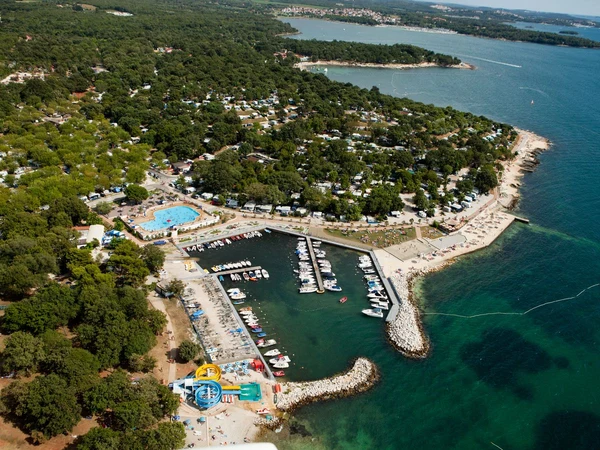 Aerial view of a marina filled with boats, adjacent to a swimming pool and surrounding forested camping area at Zelena Laguna