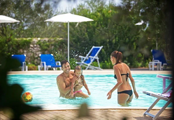 A family plays joyfully in a swimming pool, surrounded by trees and lounge chairs at Porto Cesareo Camping