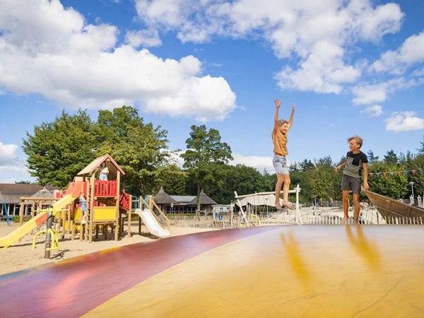 Children jumping on an inflatable cushion beside a colorful playground under a bright blue sky at Marvilla Parks Kaatsheuvel