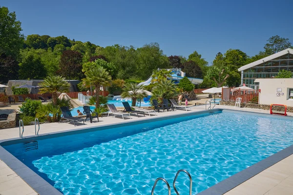 Swimming pool with sun loungers beside a water slide, surrounded by lush greenery and buildings at Marvilla Parks Le Ty Nadan