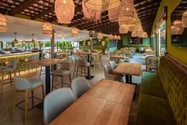 Tables and chairs arranged in a cozy, green-themed restaurant with woven pendant lights and a bar counter at Enmar
