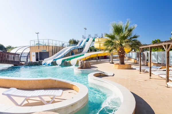 Water park slides descend into a swimming pool surrounded by lounge chairs and a palm tree at Marvilla Parks Le Soleil de la Mediterranee