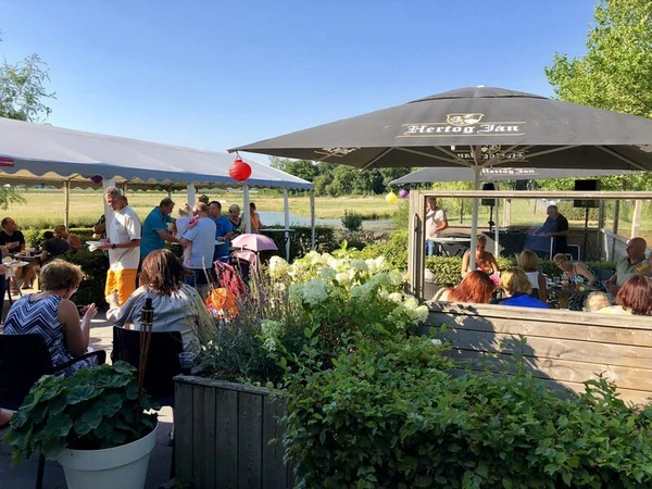 People eating and socializing under umbrellas and tents, surrounded by plants and greenery at Betuwe