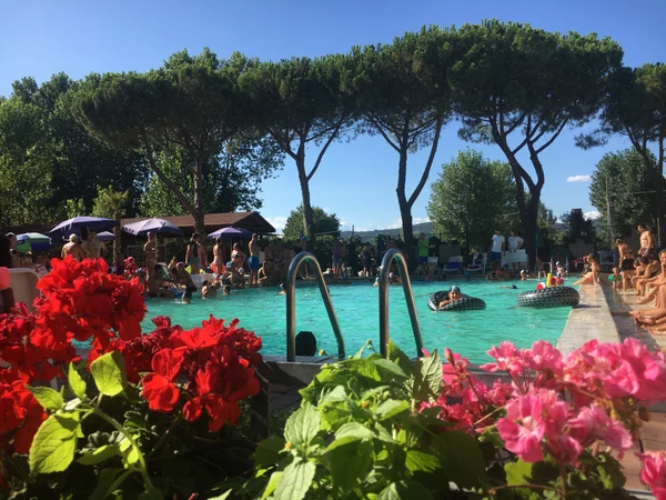 People enjoying a crowded swimming pool, surrounded by trees and flowers, with inflatables and playful socializing at Punta Navaccia