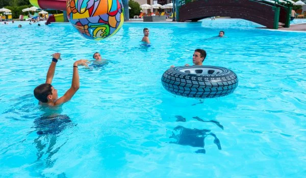 Children playing with colorful inflatables in a pool, surrounded by others swimming and a footbridge in the background at Residence Eden
