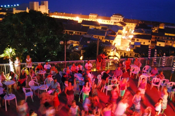 People sitting and dancing on a terrace with tables and chairs, overlooking a lit town at night at Sant' Anna Residence