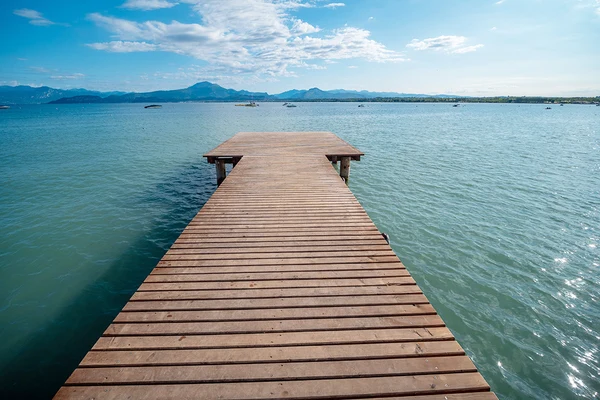 Wooden dock extending into a calm lake, mountains visible in background under a bright sky at Bella Italia