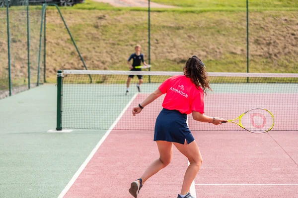 Person in pink shirt playing tennis on a court with a net, green field beyond at Marvilla Parks La Vallée