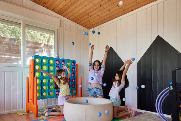 Children joyfully tossing balls indoors, surrounded by colorful play equipment and wooden-paneled walls at Taïga Delta De L'Ebre