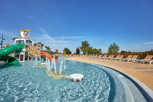 Water playground with slides and fountains, surrounded by lounge chairs and trees, against a clear blue sky at Marvilla Parks La Vallée