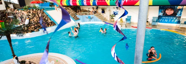 People swim and play in an indoor pool with colorful decorations and rock features at Dancamps Nordsø