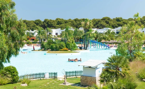 Group of people swimming in a large pool surrounded by greenery and buildings at I Turchesi Club Village