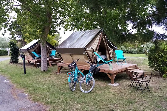 Tents stand on wooden platforms, flanked by trees; two bicycles are parked in front at Seasonova Ile de Ré