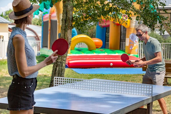 Two people play ping pong outdoors near colorful inflatable play structures at Les 2 Fontaines