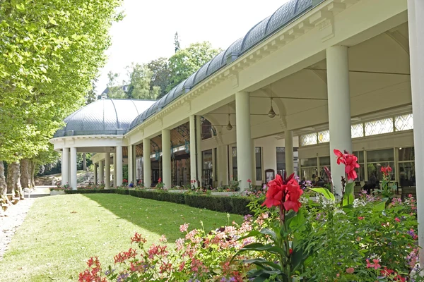 Building with a curved roof and columns surrounded by lush gardens, path, and trees at Seasonova Vittel
