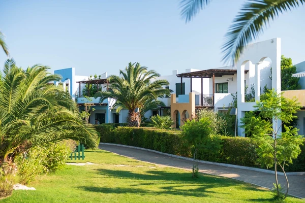 White Mediterranean-style buildings with balconies amidst palm trees and lush greenery under a clear blue sky at I Turchesi Club Village